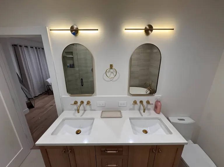 Finished bathroom with a double vanity, wall-mounted gold faucets and arched mirrors